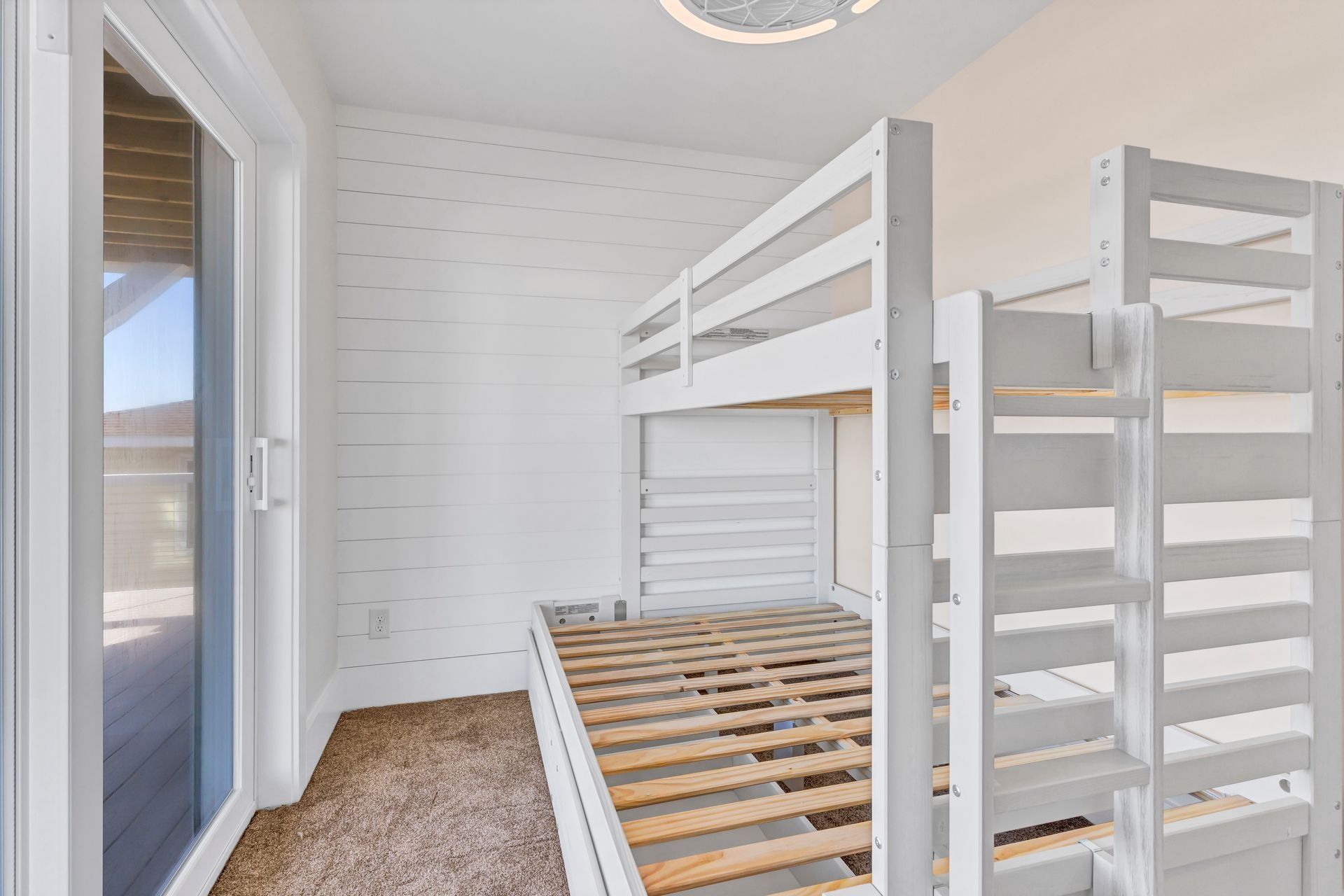 White bunk beds in a room with a sliding glass door and carpet.