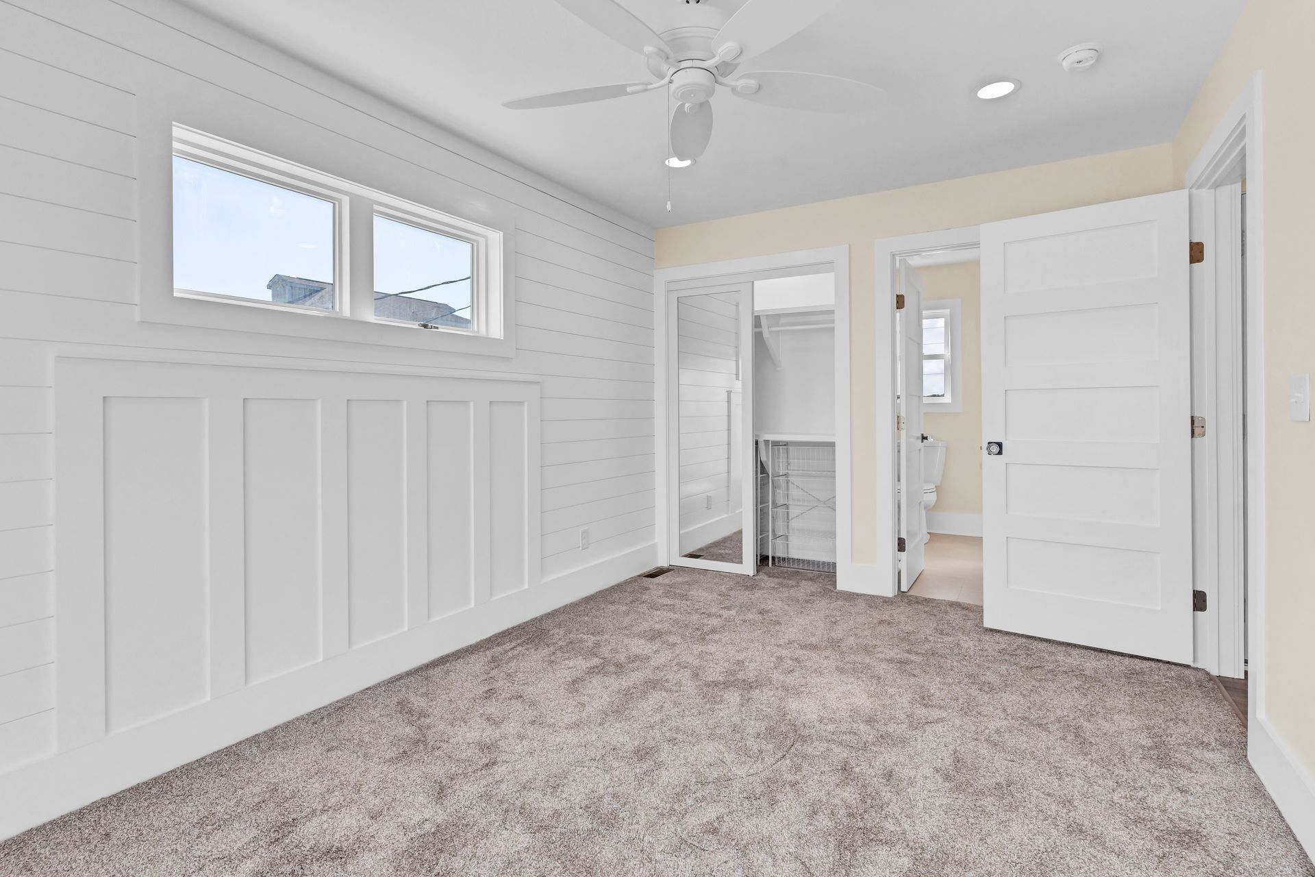 White bedroom with paneling, two windows, carpet, and two doorways leading to a walk-in closet and bathroom.