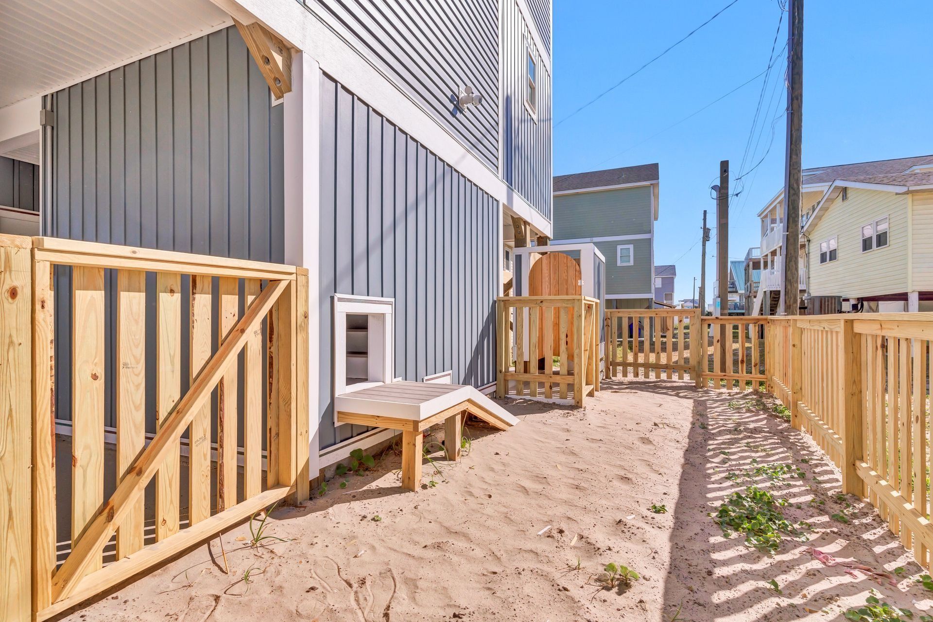 A fenced-in sandy area with a dog door and ramp, attached to a gray building.