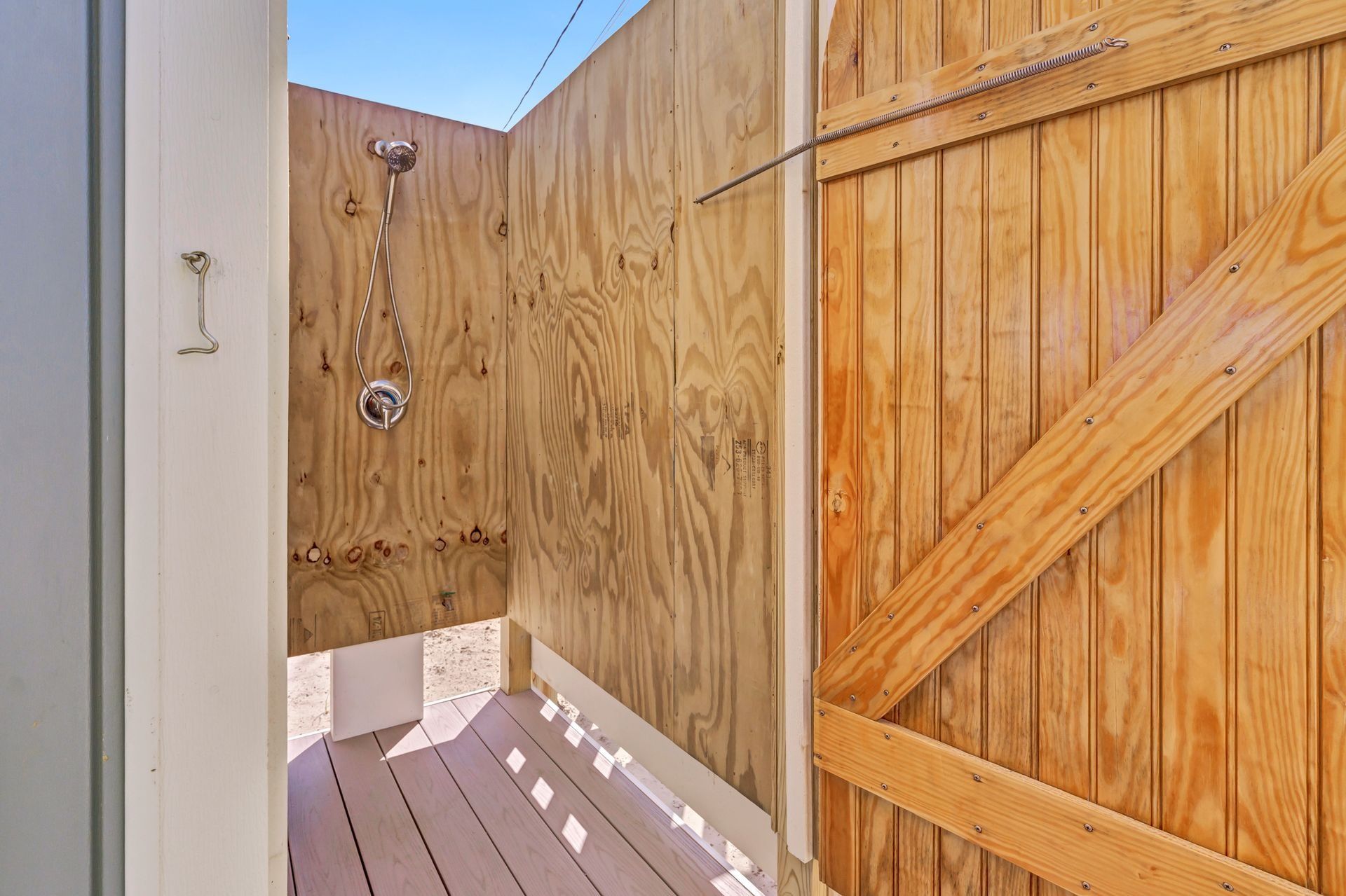 Outdoor wooden shower stall with a door and showerhead.