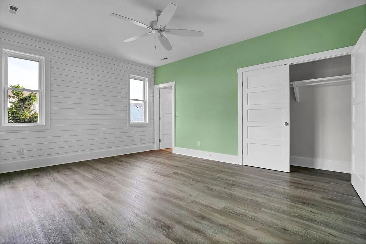 Empty bedroom with green accent wall, white trim, grey wood-look flooring, and closet.