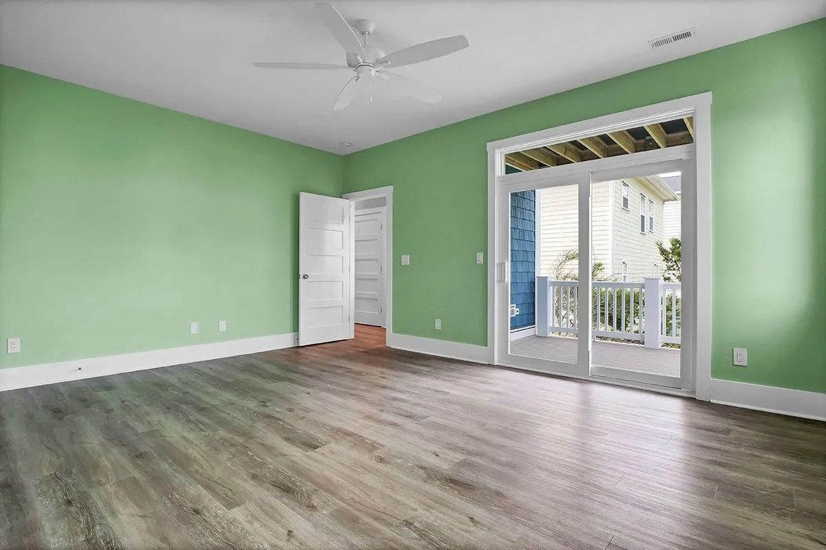 Empty bedroom with green walls, wood flooring, a white ceiling fan, and sliding doors to a balcony.