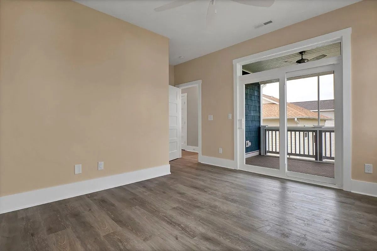 Empty room with wooden floors, tan walls, and a sliding door leading to a balcony.