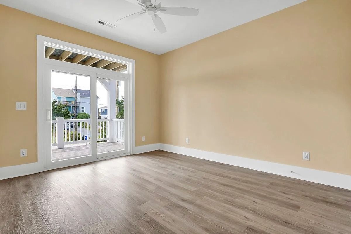 Empty room with wooden floor, tan walls, and a door to a white balcony.