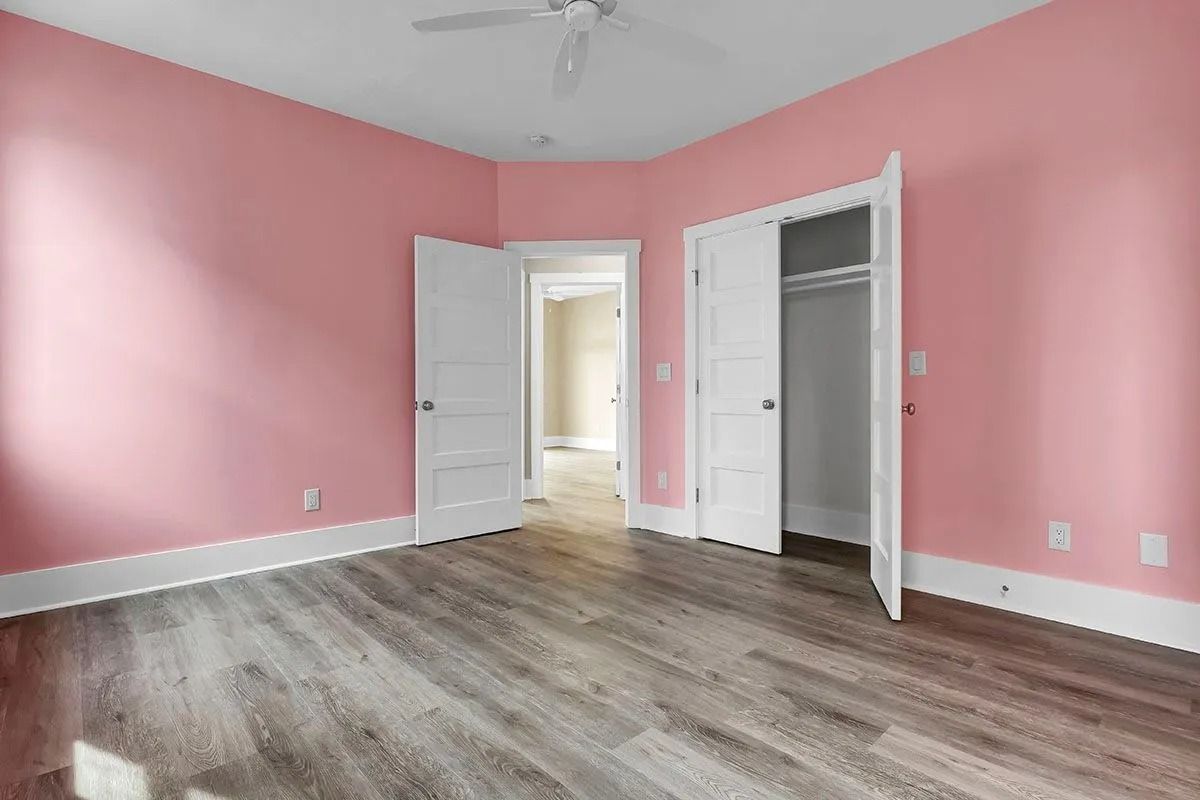 Empty bedroom with pink walls, white trim, wood-look floor, and open doors.
