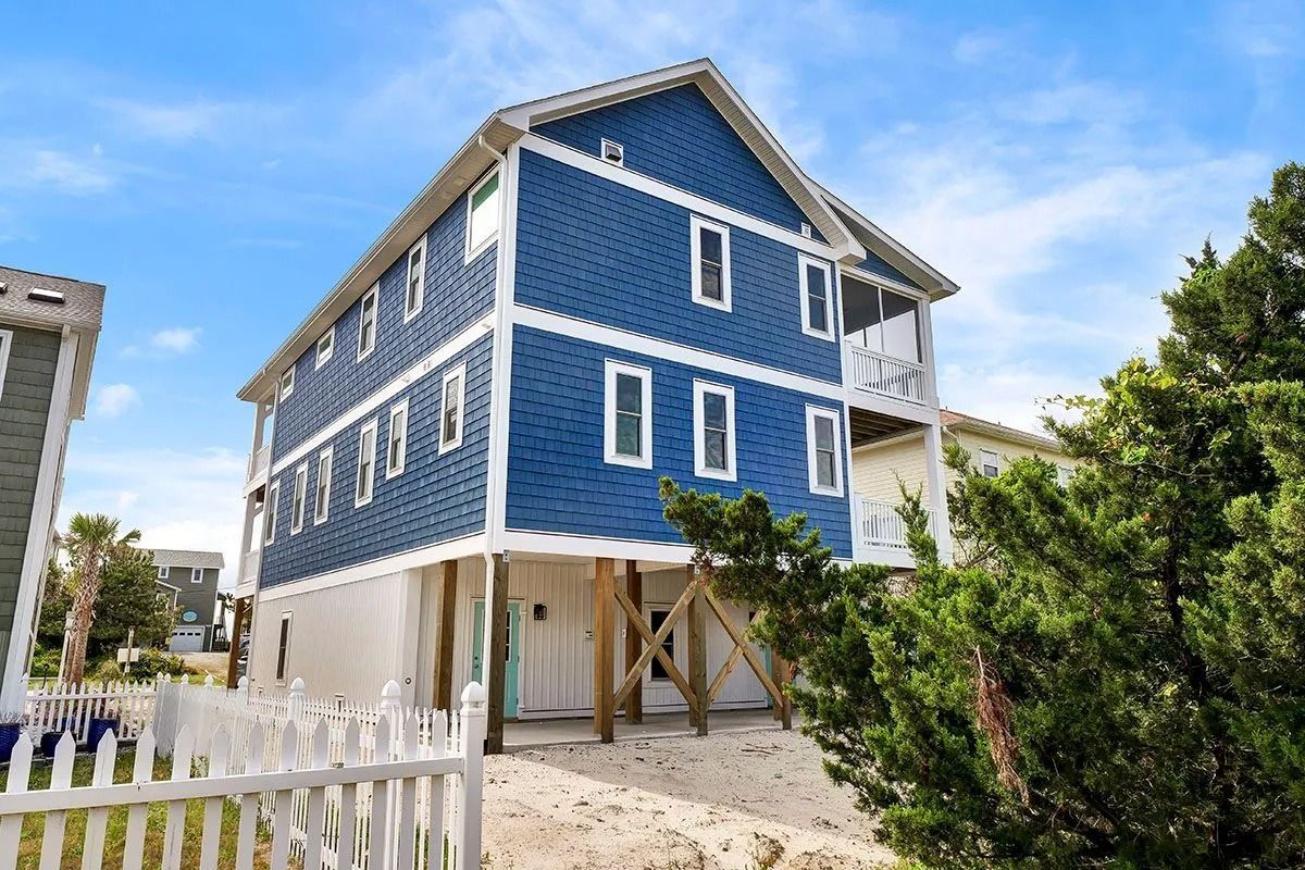Blue beach house on stilts with white trim, a screened porch, and a white picket fence.