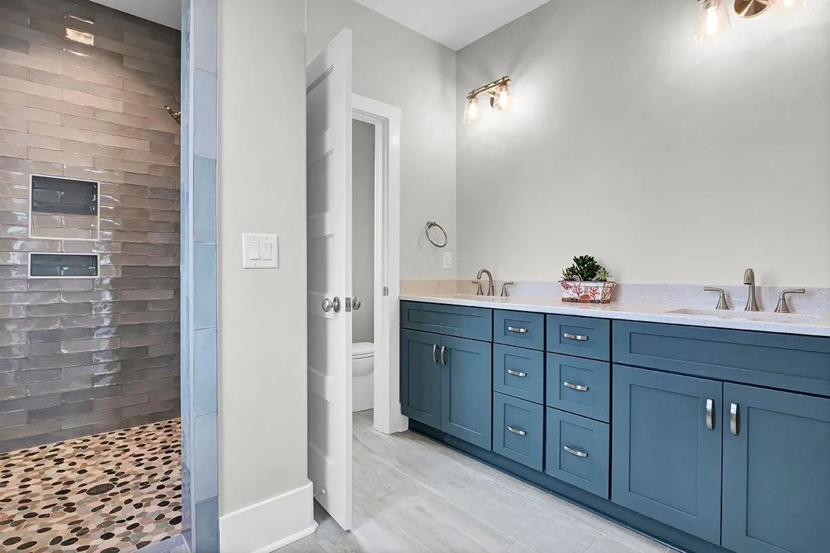Bathroom with blue cabinets, white countertops, stone shower, and open door to toilet.