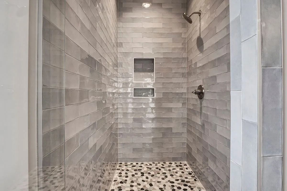 Gray-tiled shower with pebble floor, glass door, and recessed shelving.