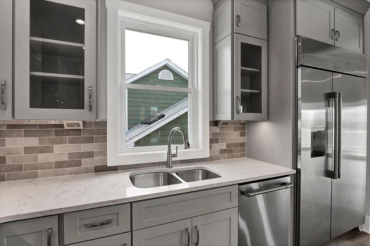 Kitchen with gray cabinets, a window, a stainless steel refrigerator, and a sink.