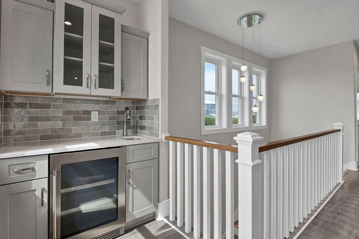 Wet bar in a home with cabinets, a mini-fridge, and a staircase with a railing.
