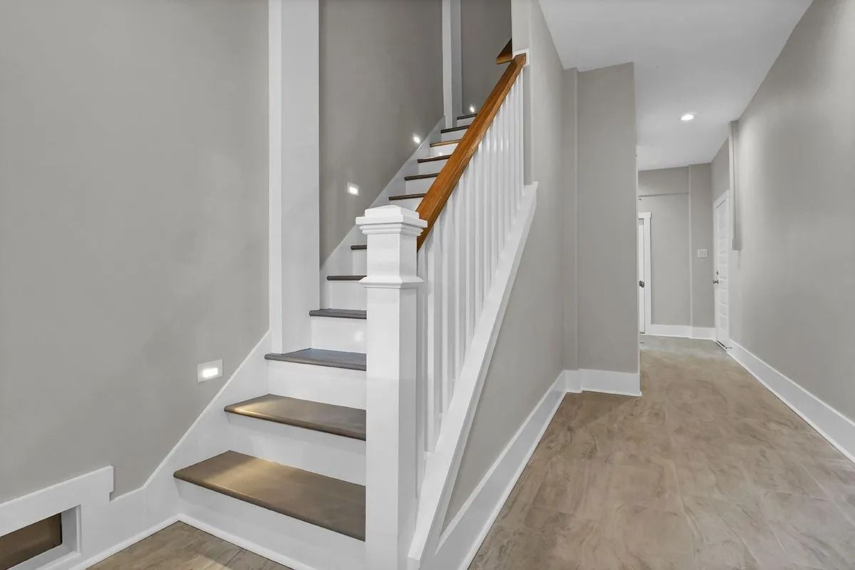 Staircase with wooden handrail, white balusters, and gray walls. Hallway with flooring to the right.