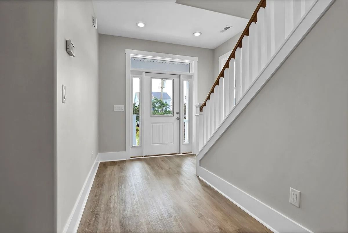 Entryway with wooden floor, white door, and staircase with white banister. Gray walls, recessed lighting.