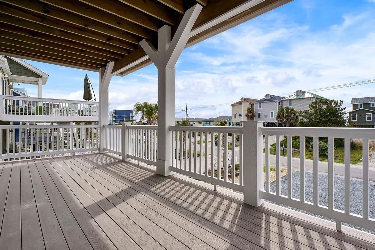 A wooden deck with white railing overlooks a neighborhood and blue sky.