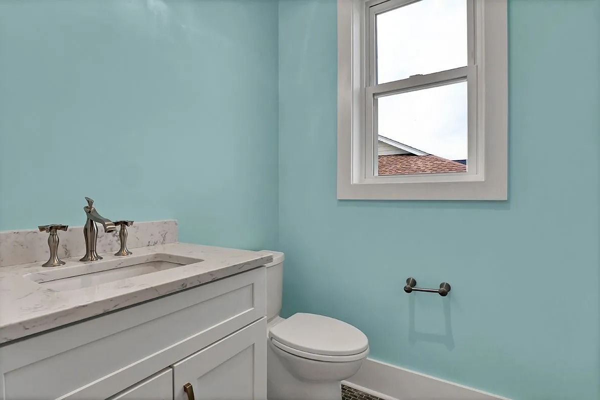 Powder blue bathroom with white vanity, toilet, and window.