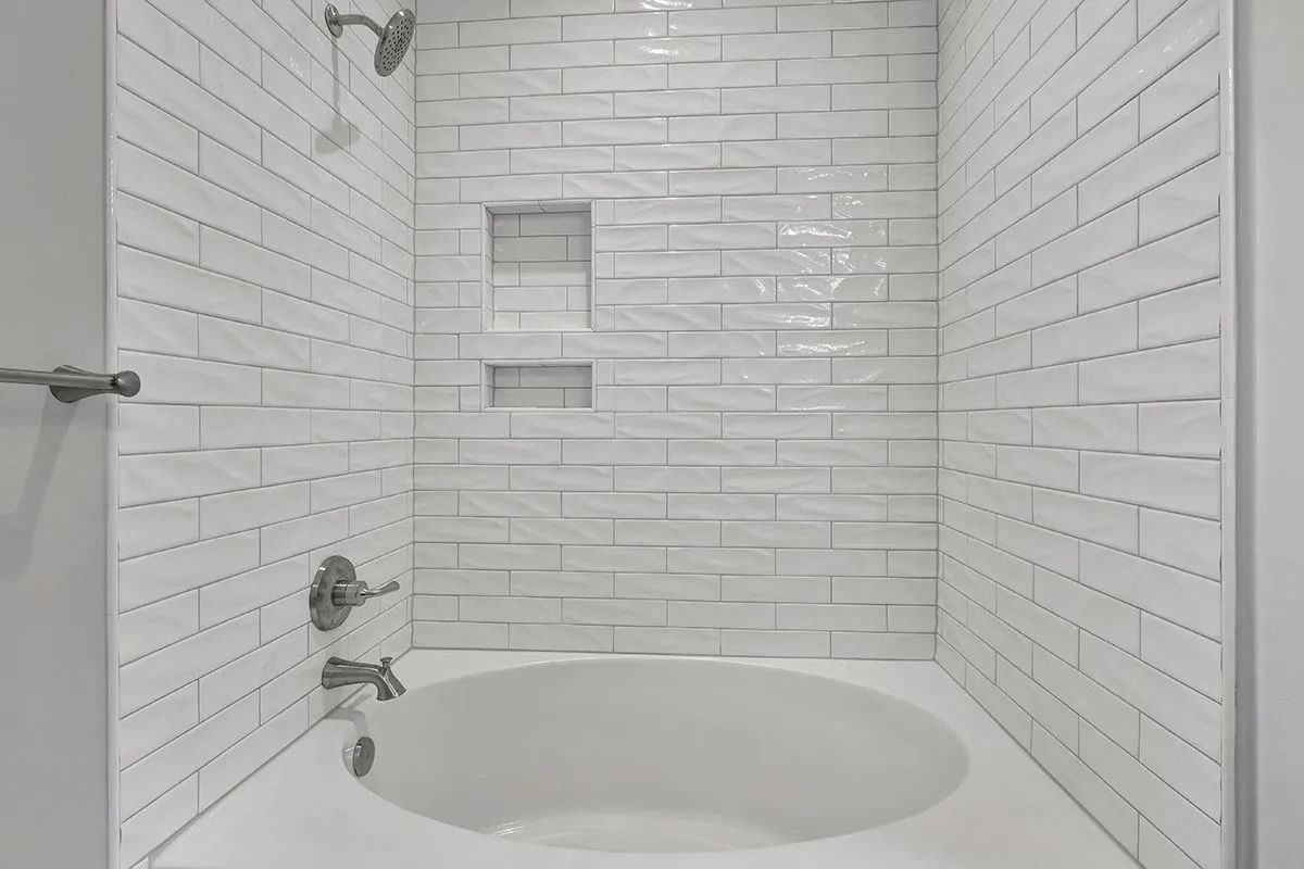 White tiled shower stall with built-in shelves and a round tub.