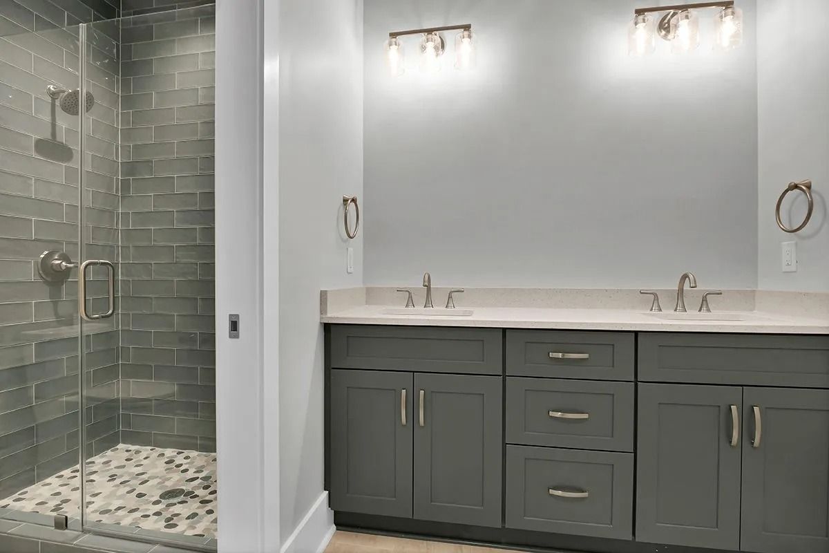 Gray bathroom with a glass shower and double vanity with gray cabinets and white countertop.