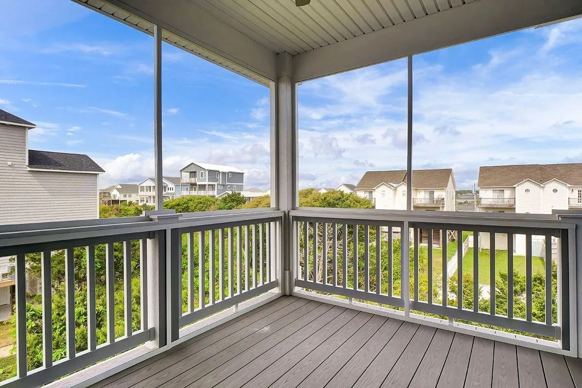 Screened porch with gray railing and floor, overlooking green trees and houses under a blue sky.