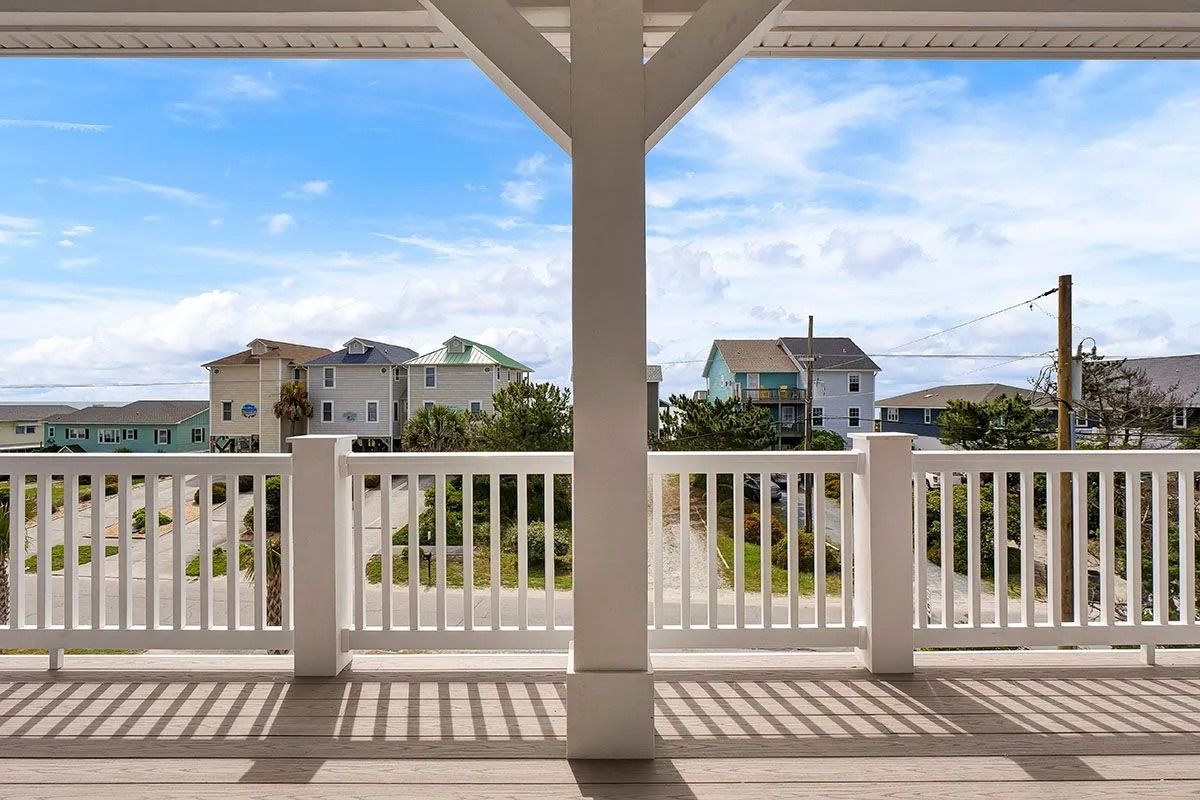 View from a porch with white railing and support beams overlooking houses and a street under a blue sky.