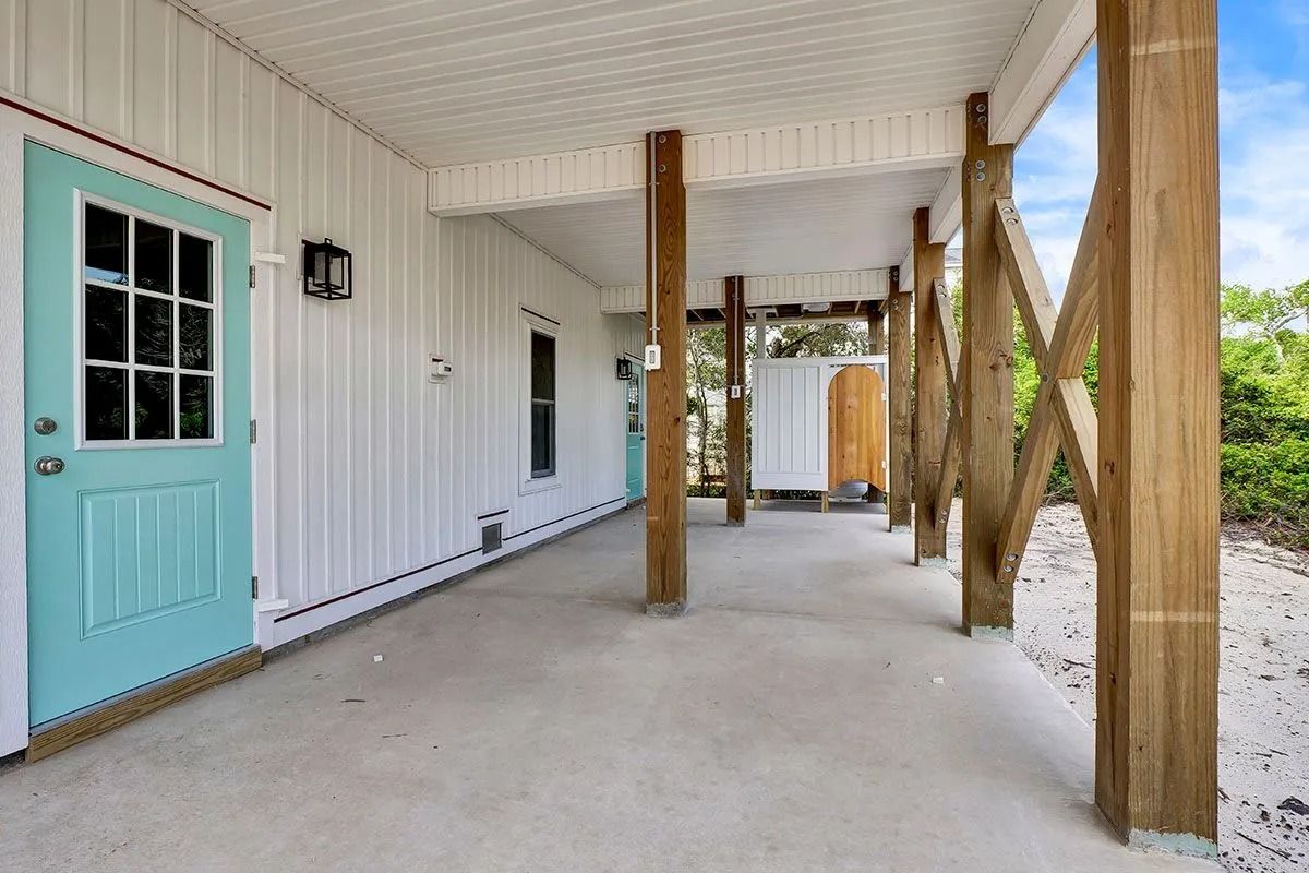 Covered porch of a beach house with turquoise door and wooden supports.