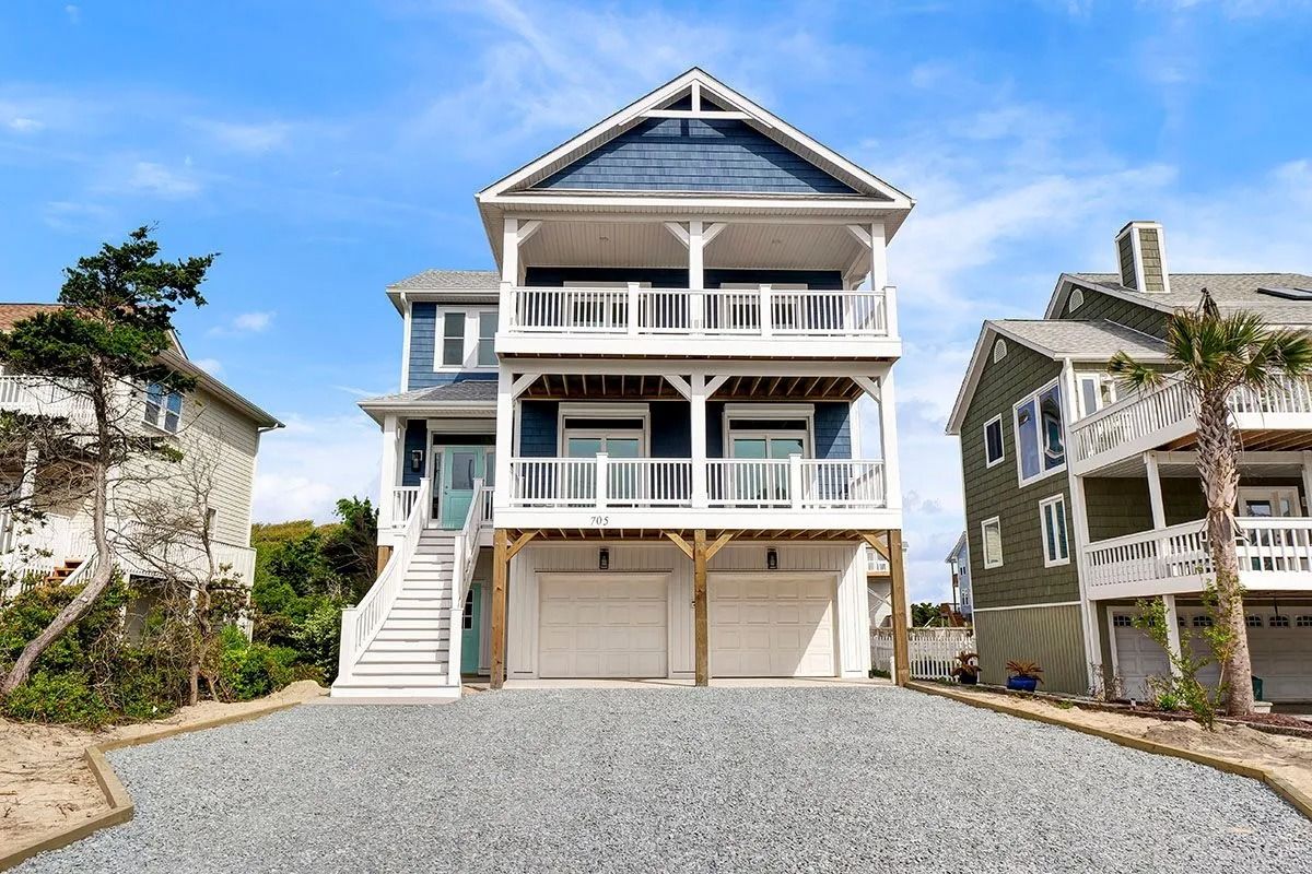 Blue and white beach house with two balconies and a gravel driveway under a blue sky.