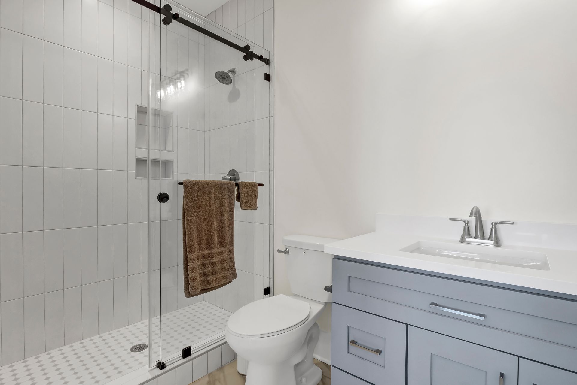 Bathroom with glass shower, white tile, blue vanity, white sink, and toilet. A brown towel hangs.
