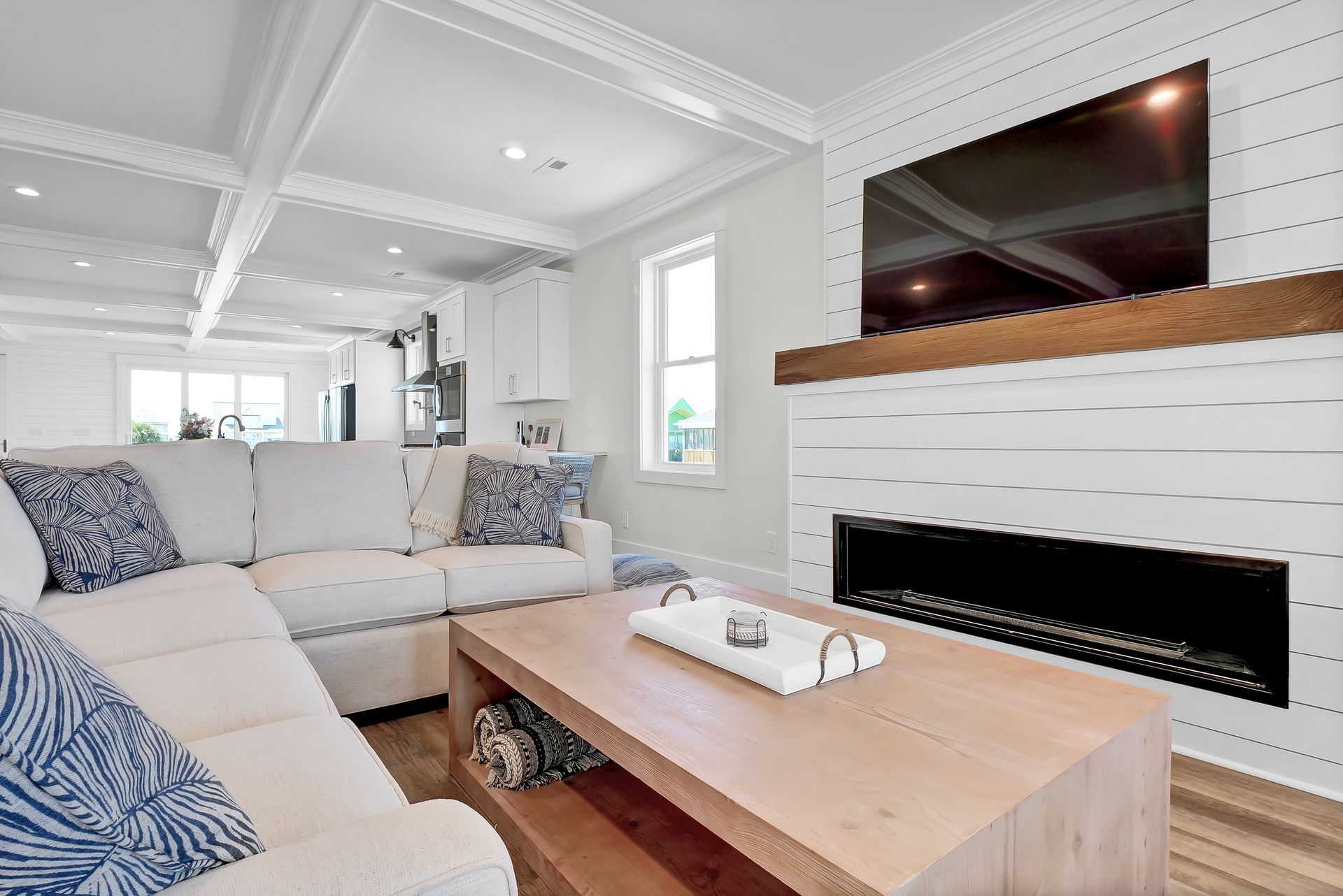 White living room with sectional sofa, fireplace with TV, and wood coffee table.
