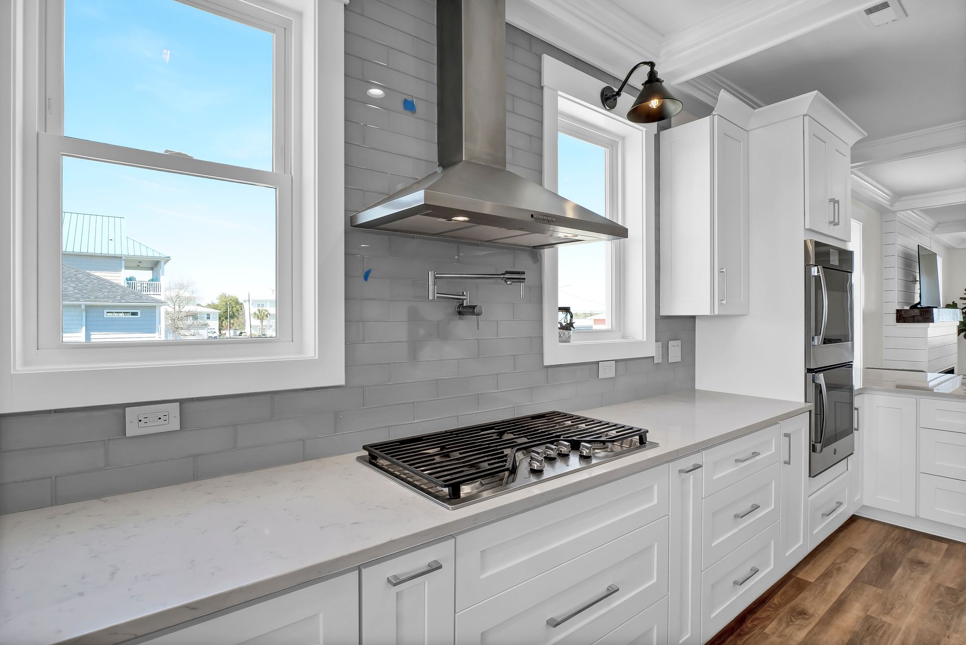 Modern kitchen with white cabinets, stainless steel range hood, cooktop, and two windows.