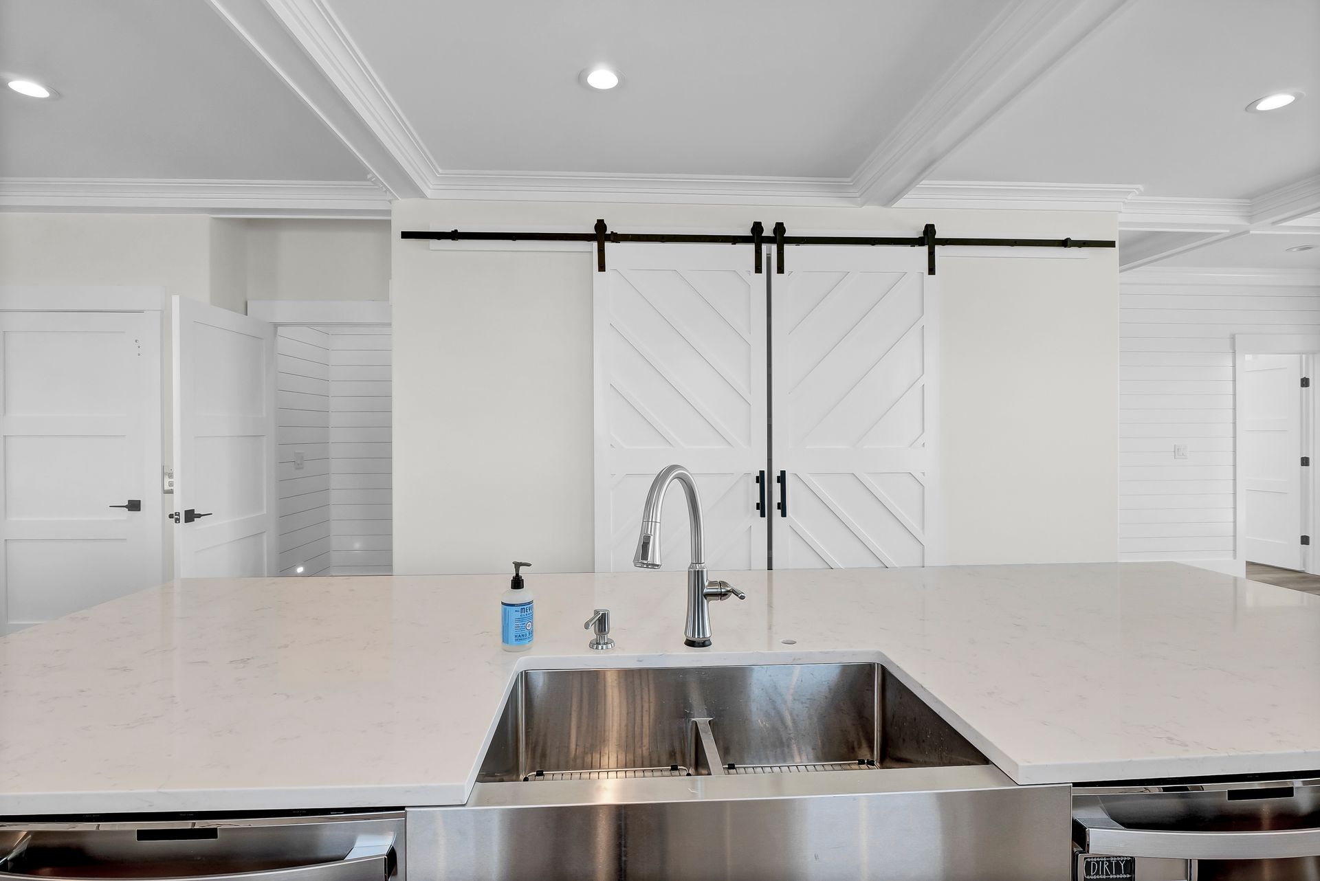 White kitchen with a stainless steel sink, countertop, and a pair of barn doors.