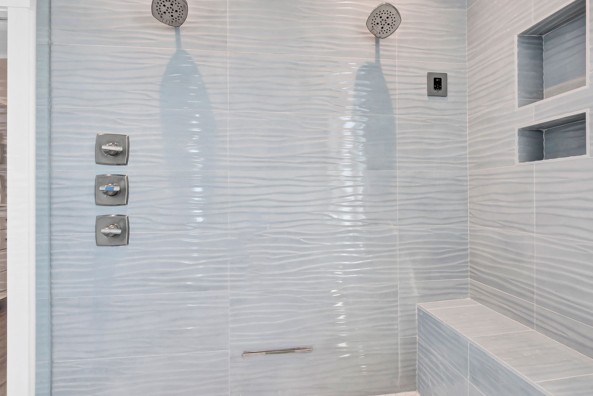 Light blue tiled shower with built-in bench, two showerheads, and recessed shelves.