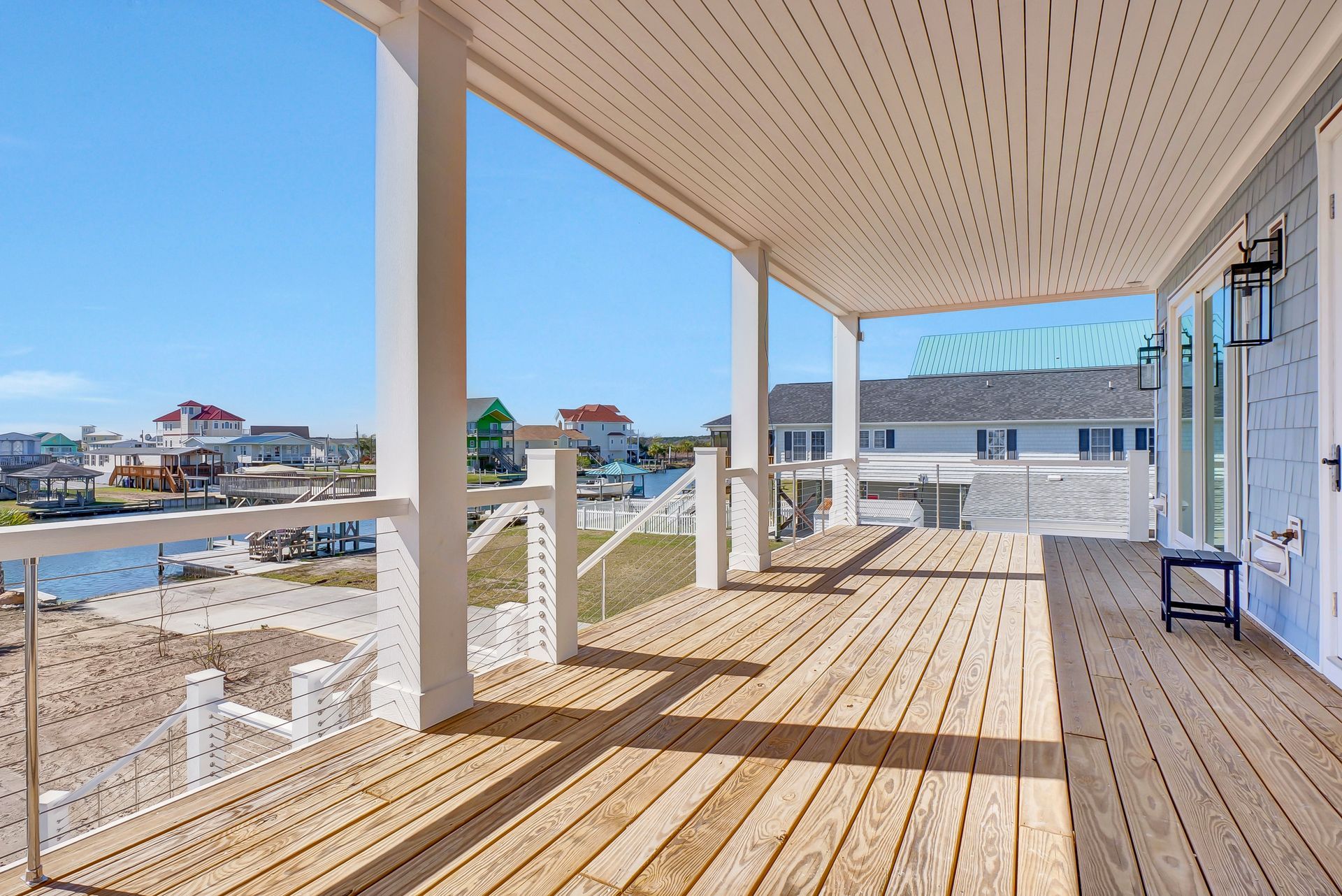 Wooden deck with water view, white columns, blue sky.