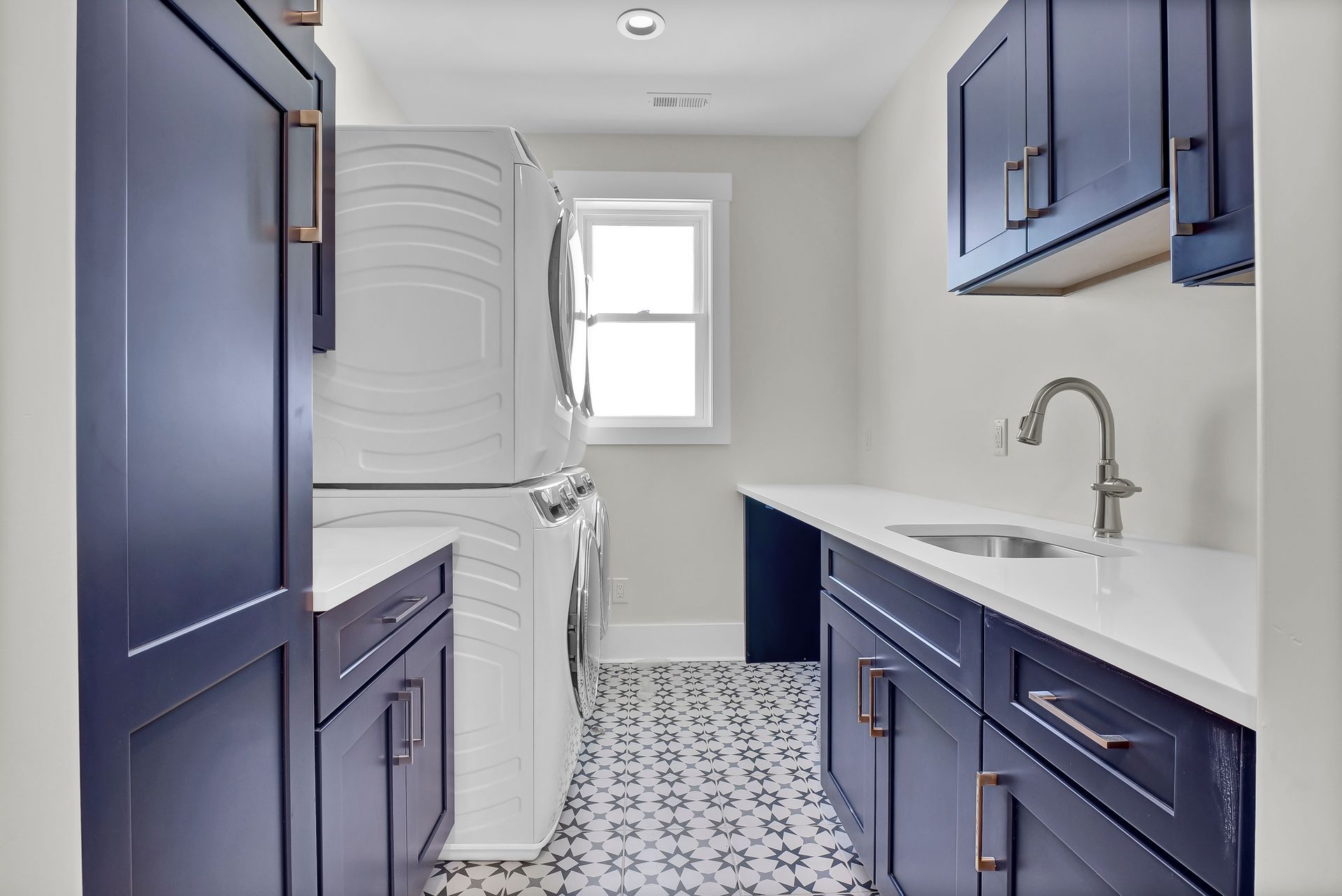 Laundry room with navy blue cabinets, white countertops, stacked washer/dryer, and patterned floor tile.