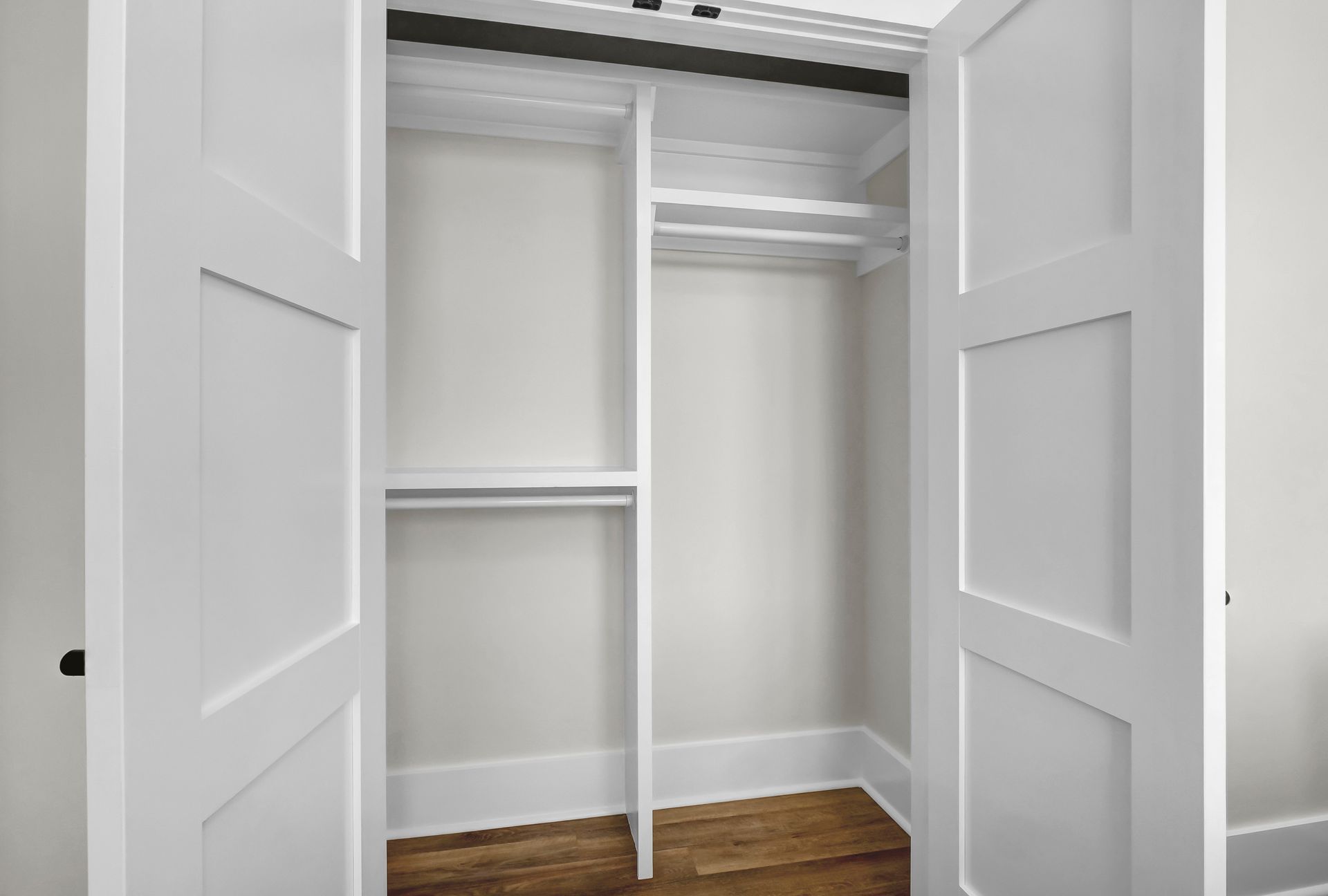 Empty white closet with open doors and built-in shelves and rods.