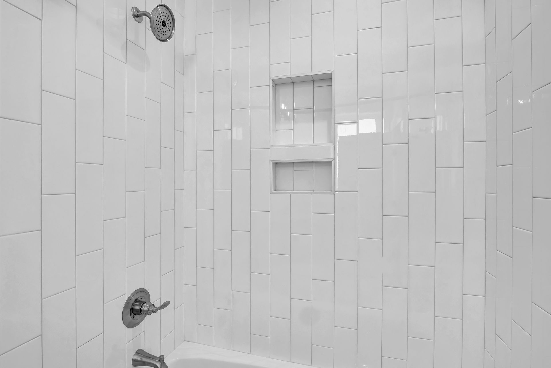 White tiled shower with built-in shelf and silver fixtures.