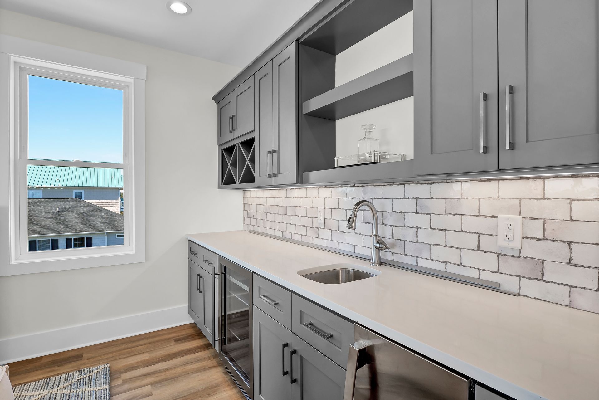 Gray home bar with cabinets, white countertop, sink, wine fridge, and brick backsplash.