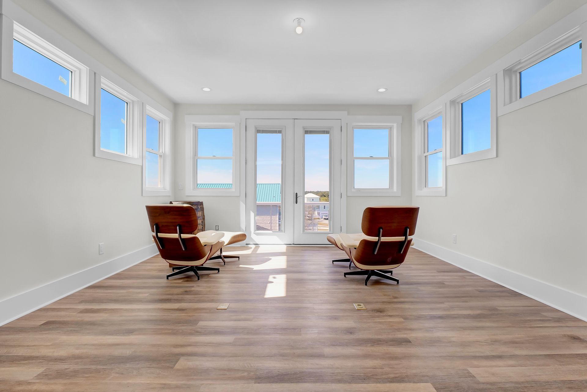 Bright room with two brown lounge chairs facing glass doors and windows, overlooking an ocean view.