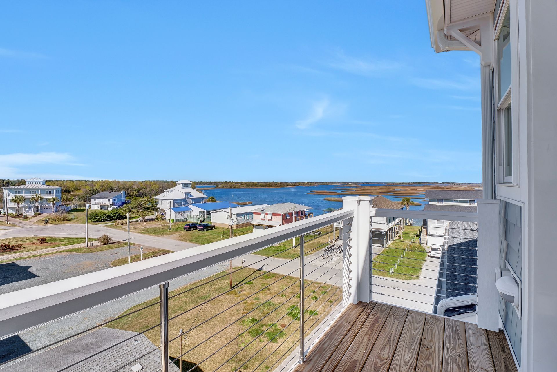 Balcony view of a coastal neighborhood with houses, water, and clear blue sky.