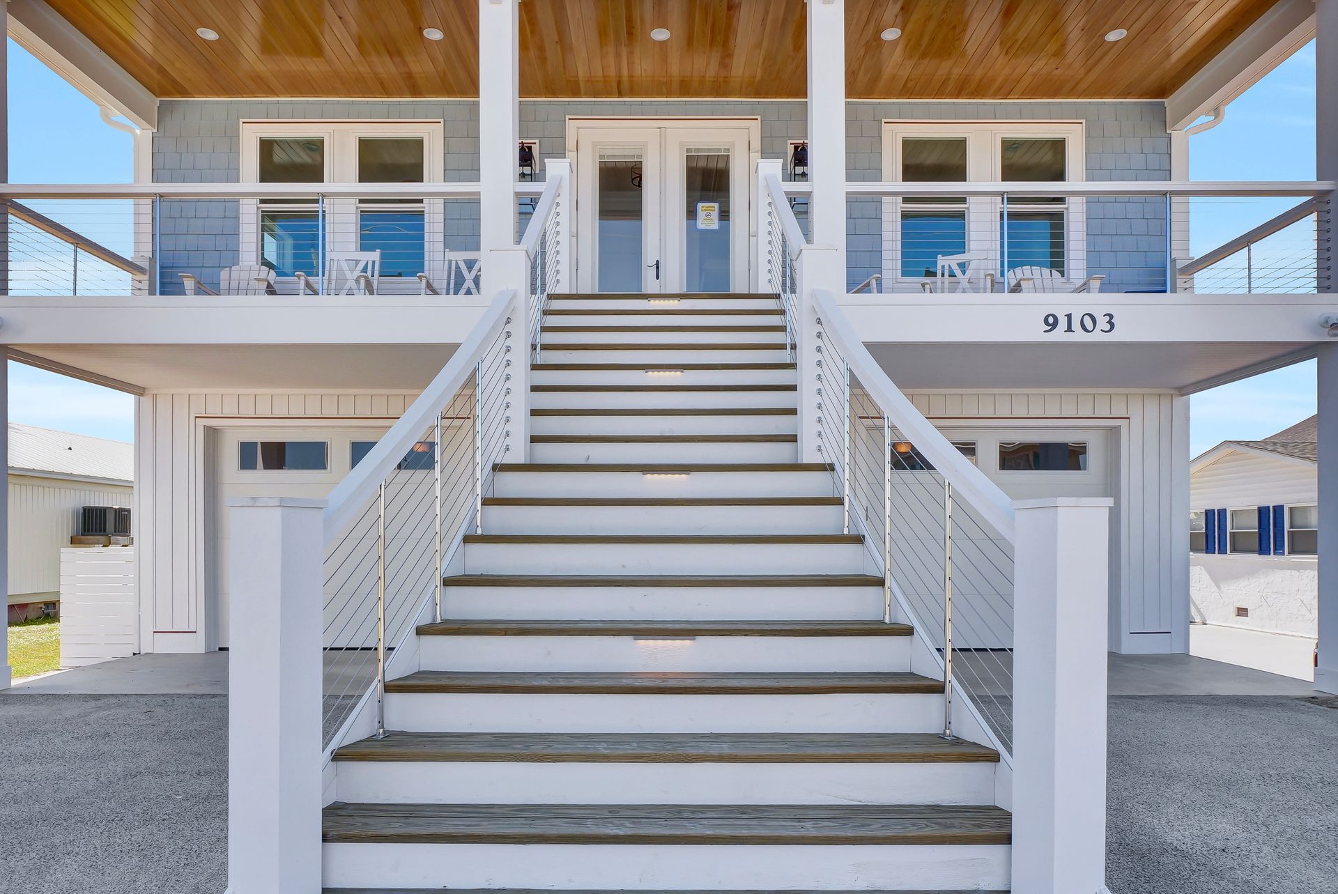 White beach house with long staircase, blue siding, garage, and open deck.