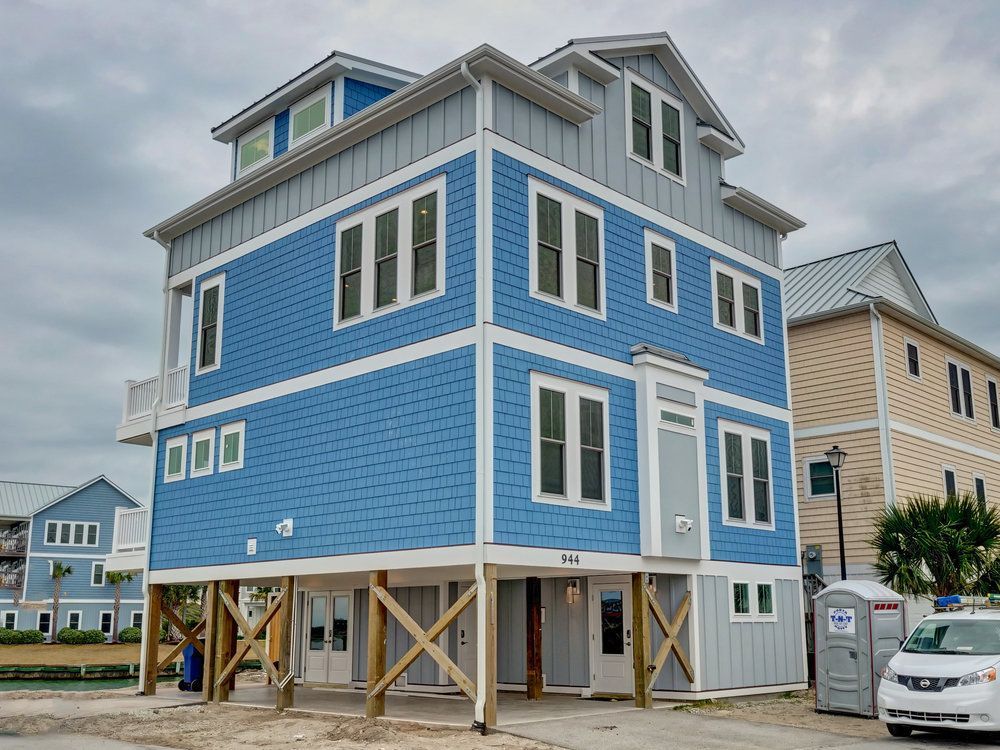 Blue and gray multi-story house on stilts under a cloudy sky.