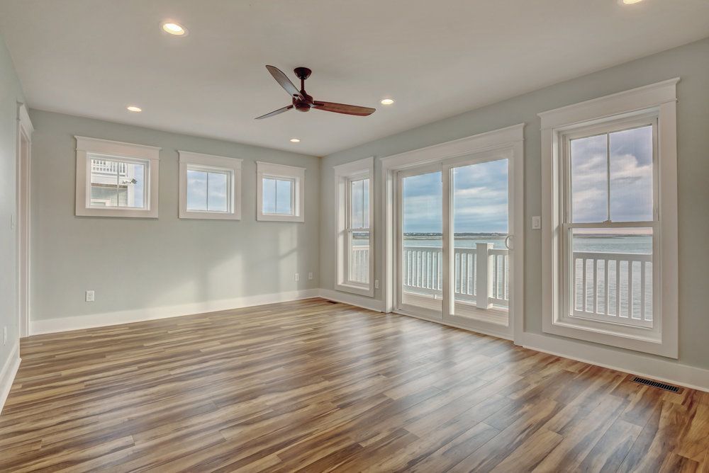 Empty room with hardwood floors, light blue walls, and ocean view from windows and sliding doors.