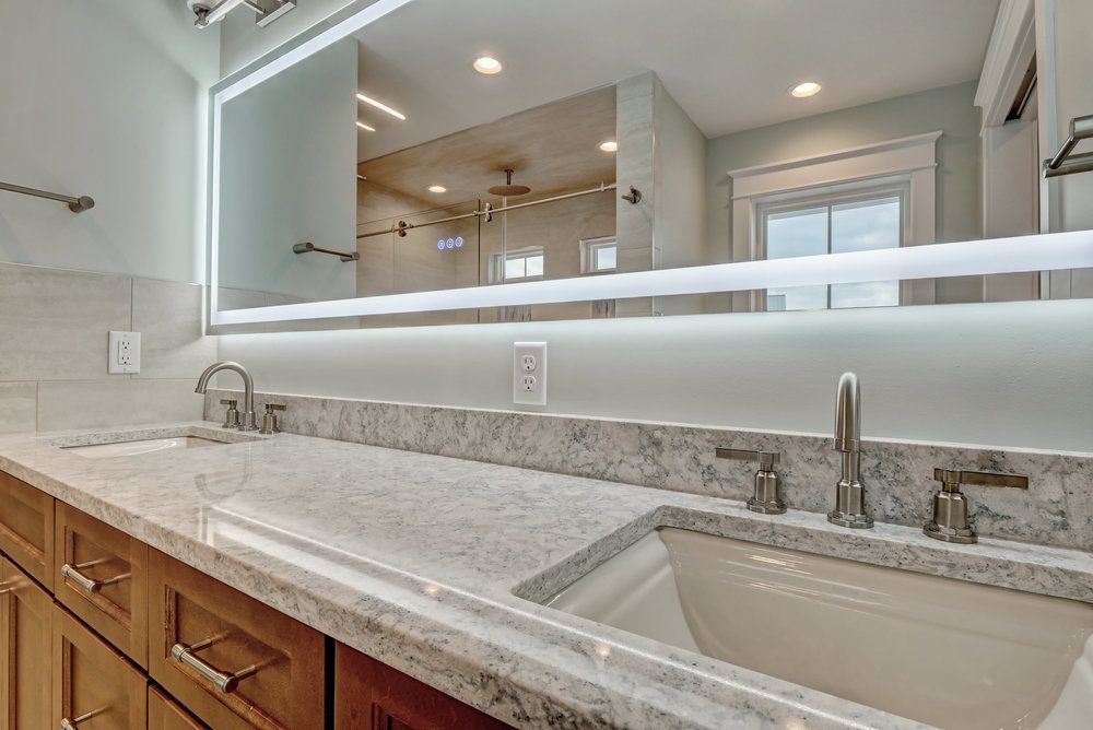 Bathroom with double sinks, a lit mirror, a granite countertop, and wooden cabinets.