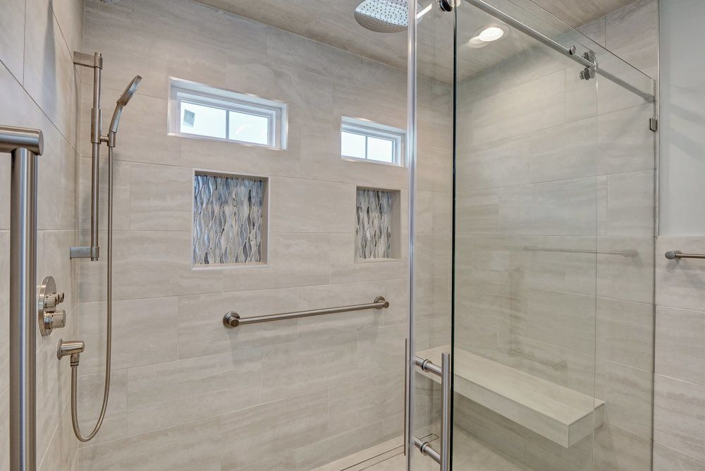 Modern bathroom with glass shower, gray tiles, and a built-in bench. Includes a handrail and shower head.