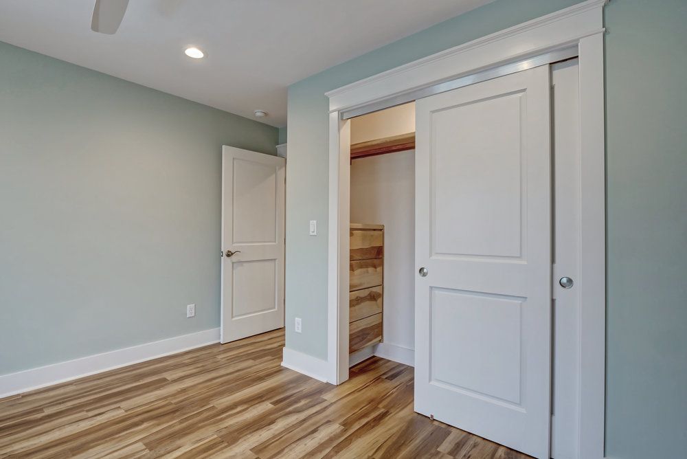 Bedroom with blue-green walls, wood floors, white doors, and a sliding closet.