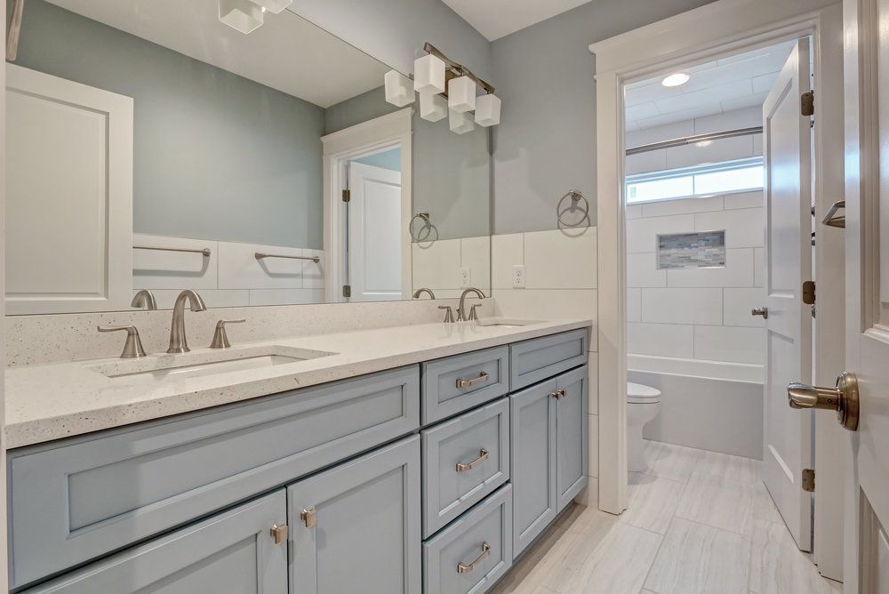 Bathroom with light blue cabinets, white countertops, double sinks, and a large mirror.