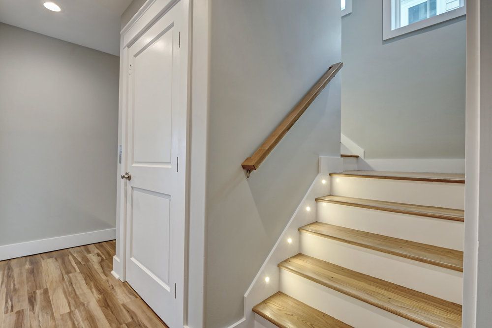 Interior view of a staircase with built-in lights, wooden steps, and a white door in a neutral-colored hallway.