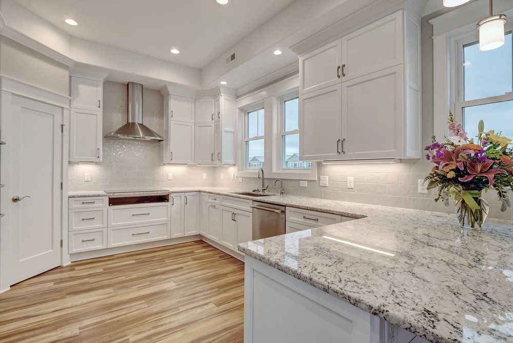 White kitchen with granite countertops, stainless steel appliances, and wood flooring.