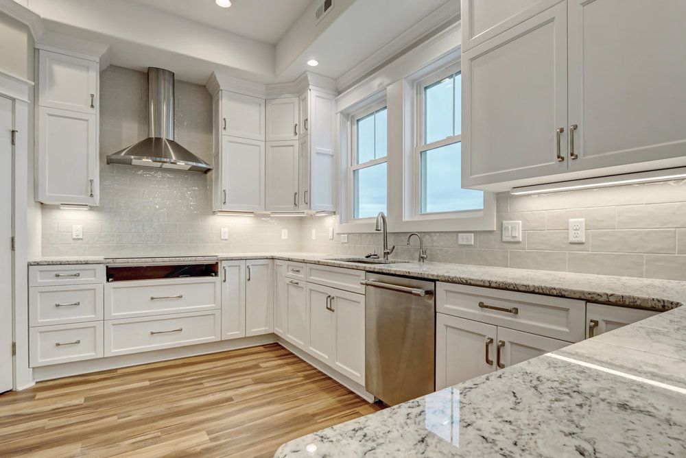 White kitchen with stainless steel appliances, granite countertops, and light wood flooring.