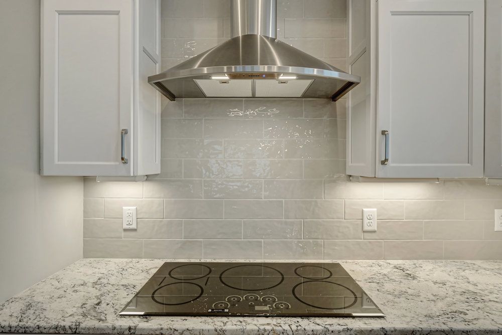 Kitchen with stovetop, range hood, white cabinets, and gray backsplash.