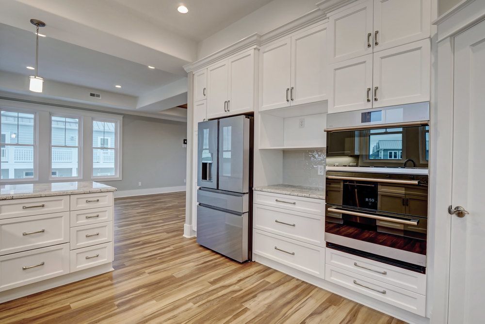 White kitchen with stainless steel appliances, marble countertops, and light wood flooring.