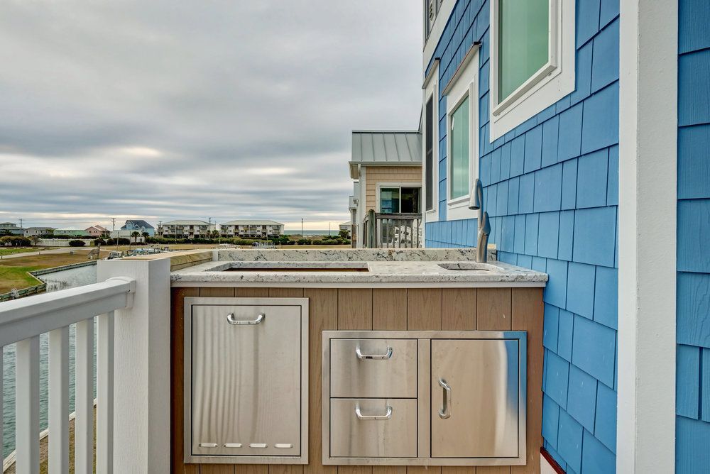 Outdoor kitchen with stainless steel appliances and blue siding on a balcony overlooking water.