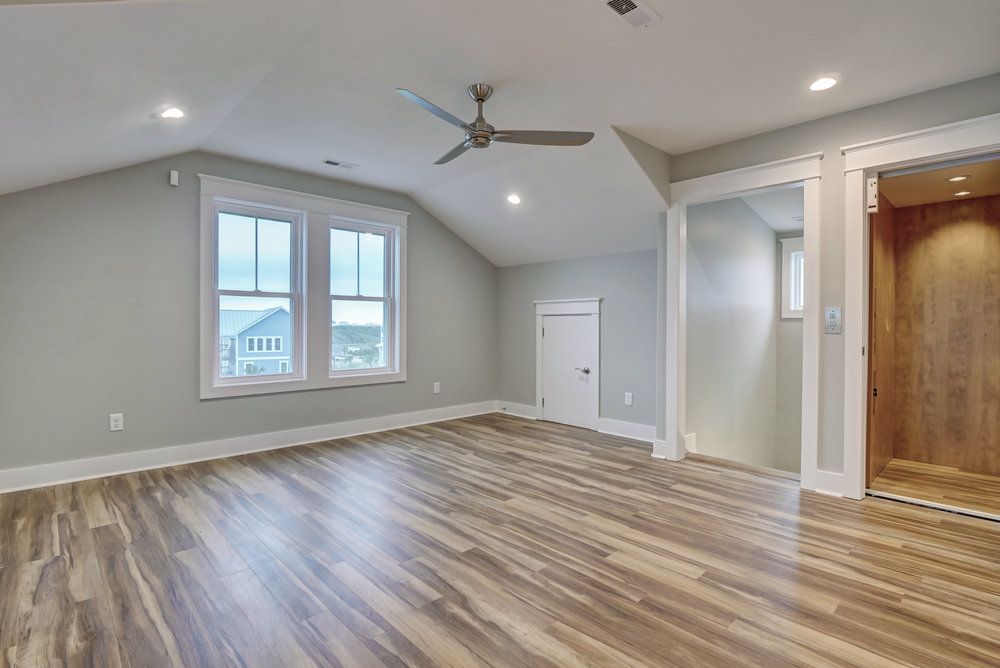 Empty room with gray walls, wood-look flooring, windows, and an elevator.